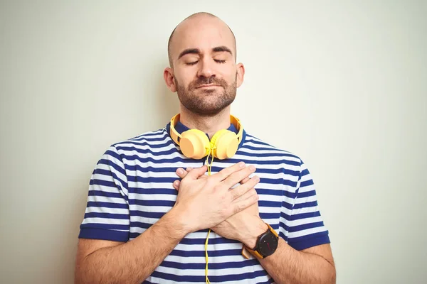 黄色いヘッドフォンを着て音楽を聴いている若者は 目を閉じて感謝のジェスチャーで胸に手を当て 孤立した背景の上に微笑んでいます 健康の概念 — ストック写真