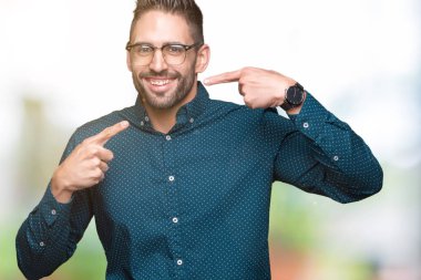 Kendinden emin gösterilen ve işaret parmakları diş ve ağız ile gülümseyen izole arka plan üzerinde gözlük takan genç yakışıklı iş adamı. Sağlık kavramı.