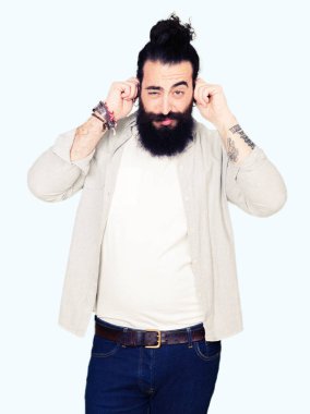 Uzun saç, sakal ve yüksek sesle müzik gürültü rahatsız ifade parmaklarıyla kulaklarıyla kapsayan küpe olan genç adam. Sağır kavramı.