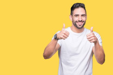 El ile pozitif jest yapıyor izole arka plan başarı işareti üzerinde rahat beyaz t-shirt giyen genç adam başparmak gülümseyen ve mutlu. Neşeli bir ifadeyle, kazanan jest kameraya bakıyor.