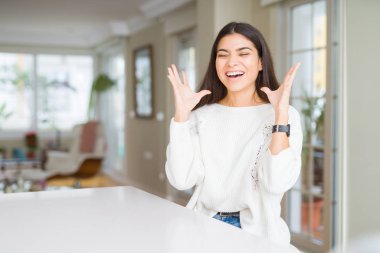 Genç güzel kadın evde beyaz masada deli ve deli kollarını kaldırdı ve kapalı gözleri heyecan çığlık ile başarı için deli kutluyor. Kazanan kavramı