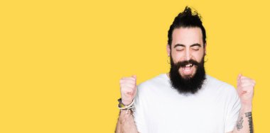 Uzun saç ve sakal casual beyaz t-shirt silah ile başarı için heyecanlı giyen genç hipster adamla zafer kutluyor gülümseyen kaldırdı. Kazanan kavramı.