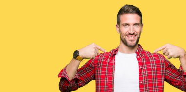 Yüzünde gülümseme ile kendinden emin görünüyorsun, kendini gururlu ve mutlu parmakları ile işaret rahat gömlek giymiş yakışıklı adam.