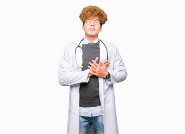 Tıbbi ceket ile gülümseyen giyen genç yakışıklı Doktor adam kapalı gözler ve yüzünde minnettar jest ile göğüs üzerinde eller. Sağlık kavramı.