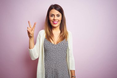 Genç güzel kadın pembe izole arka plan üzerinde duran gösteren ve emin ve mutlu gülümserken parmakları ile iki numara işaret.