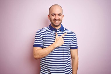 Sakallı genç kel adam pembe izole arka plan üzerinde rahat çizgili mavi t-shirt giyen yüzünde mutlu ve doğal ifade ile yan yana el ve parmak işaret yüz bir gülümseme ile neşeli