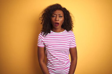 Genç Afro-Amerikan kadın izole sarı arka plan üzerinde çizgili t-shirt giyen korkmuş ve sürpriz ifade, korku ve heyecanlı yüz ile şok.
