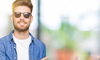 Genç yakışıklı zarif adam giyen denim ceket gülümseyen ve iki elleri ve parmakları ile tarafına işaret kamera bakıyor.