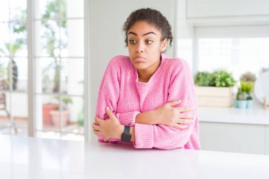 Beautiful african american woman with afro hair wearing casual pink sweater shaking and freezing for winter cold with sad and shock expression on face clipart