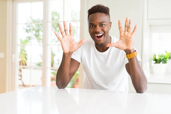 自宅の白いテーブルの上のハンサムなアフリカ系アメリカ人男性は 自信を持って幸せに微笑みながら 指番号10で見せ 指を上げる — ストック写真