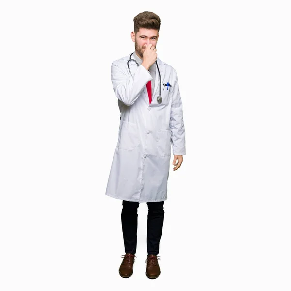 Young Handsome Doctor Man Wearing Medical Coat Smelling Something Stinky — Stock Photo, Image