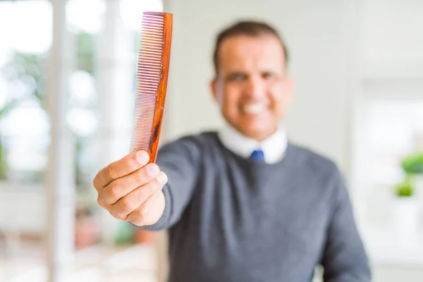 Homem de meia idade segurando e mostrando pente de cabelo enquanto sorrindo para th — Fotografia de Stock