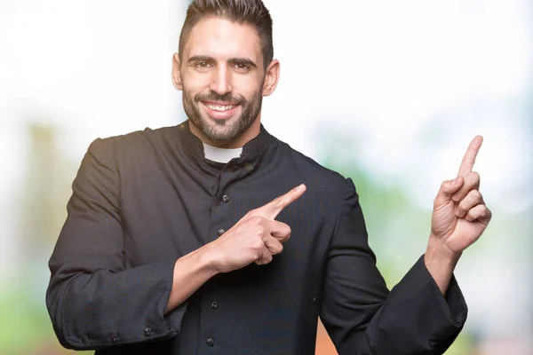 Young Christian priest over isolated background smiling and looking at the camera pointing with two hands and fingers to the side.