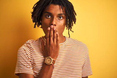 Afro adam çizgili t-shirt giyen izole sarı arka plan kapağı ağız üzerinde el hata için utanç ile şok, korku ifadesi, sessizlik, gizli kavram korkmuş