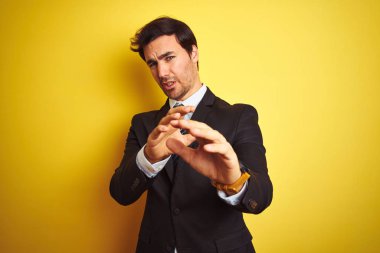 Takım elbise giyen ve kravat takan genç işadamı izole edilmiş sarı arka plan üzerinde duran tiksinti ifade, hoşnutsuz ve korkulu tiksinti yüz yapıyor çünkü nefret tepki. Elleri havada. Sinir bozucu kavram.