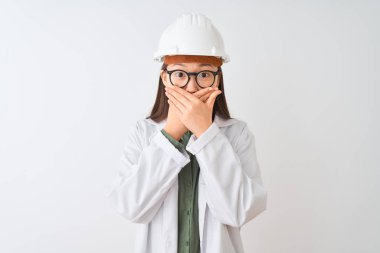 İzole beyaz arka plan üzerinde ceket kask gözlük takan genç Çinli mühendis kadın hata için elleri ile ağız kapsayan şok. Gizli kavram.