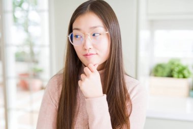 Güzel Asyalı kadın gözlük el ile çene düşünme hakkında soru, dalgın ifade üzerine. Düşünceli yüzüyle gülümsüyor. Şüphe kavramı.