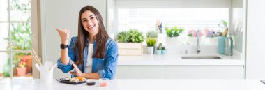 Güzel genç kadın doğum suşi yeme geniş açılı resim mutlu yüz görünümlü ve başparmak ile yan işaret gülümseyerek yukarı.