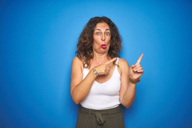 Kıvırcık saçlı orta yaş yaşlı kadın mavi izole arka plan üzerinde duran bir kenara endişeli ve sinir iki eliyle, endişeli ve sürpriz ifade