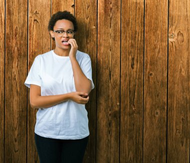 Stresli ve gergin elle çivi ısırma ağzına bakarak izole arka plan üzerinde gözlük güzel genç Afro-Amerikan kadın. Anksiyete sorunu.