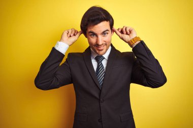 Takım elbise giyen ve kravat takan genç işadamı izole sarı arka plan üzerinde duran gülümseyerek parmakları ile kulakları çekerek, komik jest. Seçme sorunu