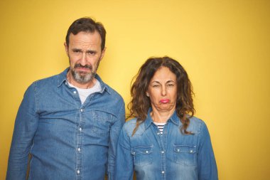 Güzel orta yaş çift birlikte izole sarı arka plan depresif üzerinde duran ve sıkıntı için endişe, kızgın ve korkmuş ağlıyor. Hüzünlü ifade.