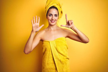Güzel kadın vücut ve baş üzerinde sarı izole arka plan üzerinde duş havlusu giyen gösteren ve parmakları ile işaret ederken emin ve mutlu gülümseyerek yedi numara.