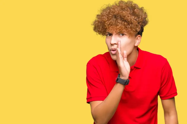 Young handsome man with afro hair wearing red t-shirt hand on mouth telling secret rumor, whispering malicious talk conversation