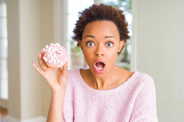 年轻的非洲美国妇女吃粉红色糖棉花糖甜甜圈害怕在震惊与惊喜的脸 害怕和兴奋与恐惧的表情 — 图库照片