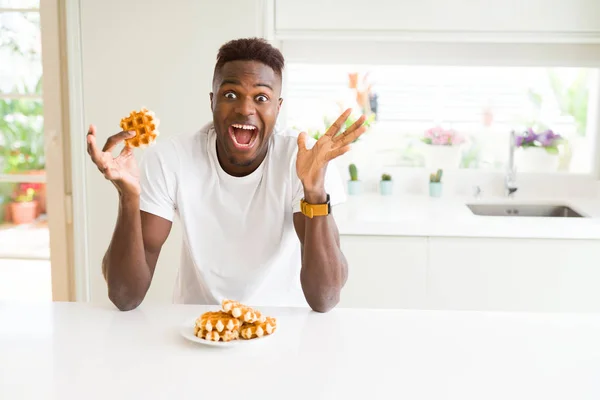 甘いベルギーワッフルを食べるアフリカ系アメリカ人男性は 大きな笑顔で叫んで勝利を祝う勝者の表情と手を上げた — ストック写真