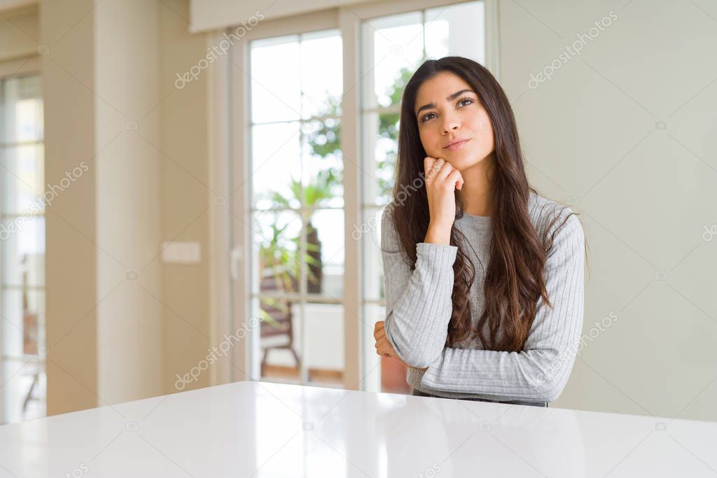 Young beautiful woman at home with hand on chin thinking about question, pensive expression. Smiling with thoughtful face. Doubt concept.