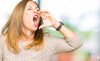 Moda kazak bağırarak ve ağzı üzerinde el ile yan için çığlık giyen güzel orta yaş kadın. İletişim kavramı.