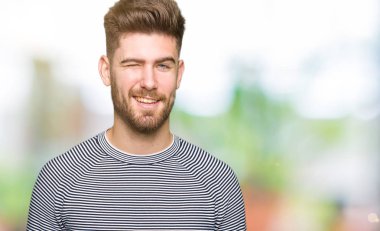 Çizgili süveter seksi bir ifadeyle, neşeli ve mutlu yüzünü kameraya bakarak göz kırpıyor giyen genç yakışıklı adam.