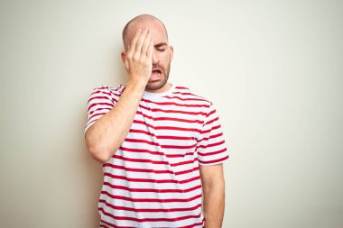 Sakallı genç kel adam beyaz izole arka plan yaslama yorgun yarım yüz kapsayan üzerinde rahat çizgili kırmızı t-shirt giyiyor, el ile göz ve ağız. Yüz acı içinde acıyor.