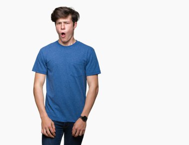 Genç yakışıklı adam izole arka plan üzerinde mavi t-shirt giyen şok yüz, şüpheci ve alaycı görünümlü, açık ağız ile şaşırttı