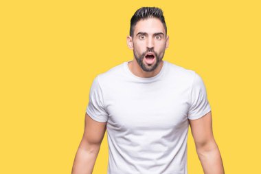 Yakışıklı adam sarı izole arka plan üzerinde beyaz t-shirt giyen şok yüzünde, şüpheci ve alaycı görünümlü, açık ağız ile şaşırttı