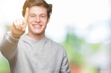Ve kendinden emin ve mutlu gülümseyerek süre parmak numaralı yukarıyı gösteren izole arka plan üzerinde sweatshirt giyen genç yakışıklı sportif adam.