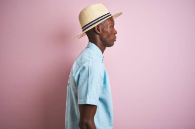 Izole pembe arka plan üzerinde mavi gömlek ve yazlık şapka giyen Afrikalı-Amerikalı adam yan bakarak, kendine güvenen gülümseme ile doğal yüz ile profil poz dinlenmek.