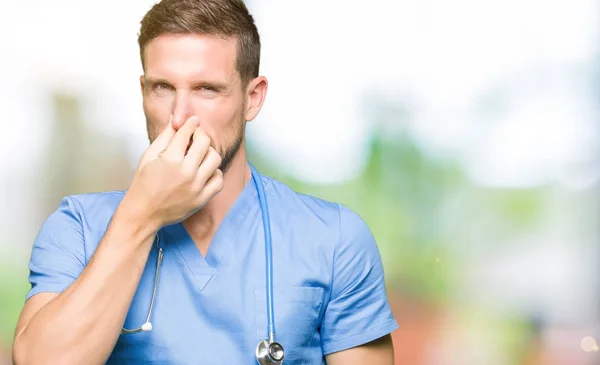 英俊的医生穿着医疗制服在孤立的背景嗅到一些臭气熏天 无法忍受的气味 屏住呼吸与手指在鼻子 难闻的气味概念 — 图库照片