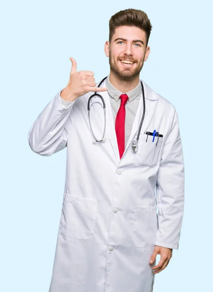 Joven Doctor Guapo Con Abrigo Médico Sonriendo Haciendo Gesto Telefónico —  Fotos de Stock