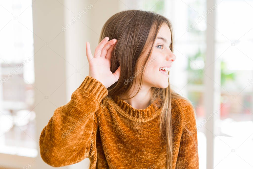Beautiful young girl kid at home smiling with hand over ear listening an hearing to rumor or gossip. Deafness concept.
