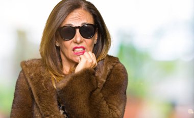 Güneş gözlüğü ve stresli ve gergin elle çivi ısırma ağzına bakarak vizon kürk giyen güzel orta yaş zarif kadın. Anksiyete sorunu.