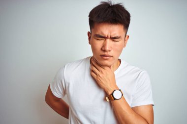 Genç asyalı Çinli adam izole beyaz arka plan üzerinde duran t-shirt giyen ağrılı boyun dokunmadan, grip, clod ve enfeksiyon için boğaz ağrısı