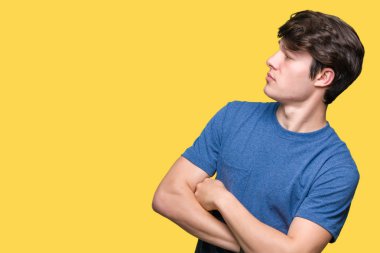 Genç yakışıklı adam üzerinde mavi t-shirt giyen izole arka plan ile yan bakarak gülümseyen ikna ve emin geçti