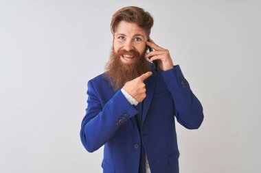 Genç kızıl İrlandalı işadamı izole beyaz arka plan üzerinde akıllı telefon üzerinde konuşurken çok mutlu el ve parmak ile işaret