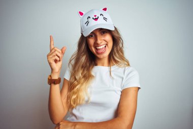 Gri izole arka plan üzerinde kedi şapkası giyen genç güzel kadın çok mutlu yan el ve parmak ile işaret