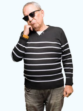 Kış lık kazak ve güneş gözlüğü takan yakışıklı erkek çenesi üzerinde soru, dalgın ifade yi düşünüyor. Düşünceli bir yüzle gülümsüyor. Şüphe kavramı.