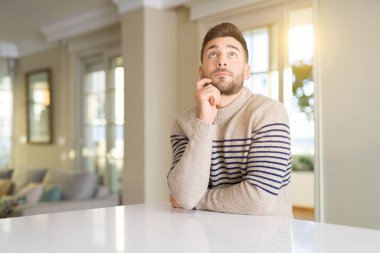 Genç yakışıklı adamla evde el çene düşünme hakkında soru, dalgın ifade üzerine. Düşünceli yüzüyle gülümsüyor. Şüphe kavramı.