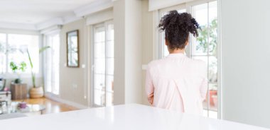 Afro saçlı güzel afro-amerikan kadın geniş açı çapraz kolları ile uzağa bakarak geriye doğru duran