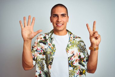 Genç yakışıklı adam tatillerde beyaz arka plan üzerinde Hawaii gömlek giyen gösteren ve emin ve mutlu gülümserken parmakları ile yedi numara işaret.